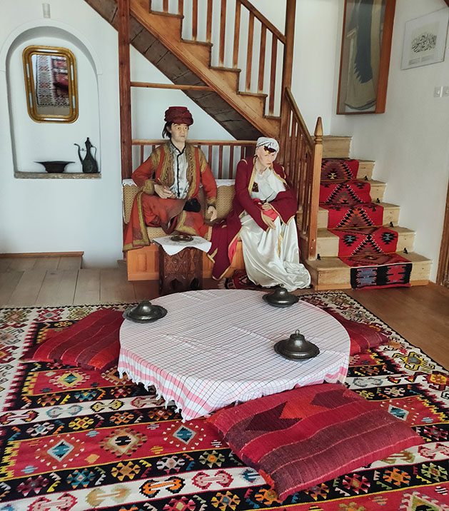 Muñecos imitando a una familia bosnia con una mesa en el suelo y alfombras en la Casa Muslibegovic - que ver en Mostar