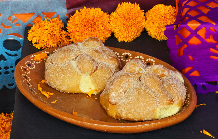 Pan de Muerto sobre un altar a modo de ofrenda junto con cempasúchil y papel picado. Este es el dulce más típico que comer en Día de Muertos en México