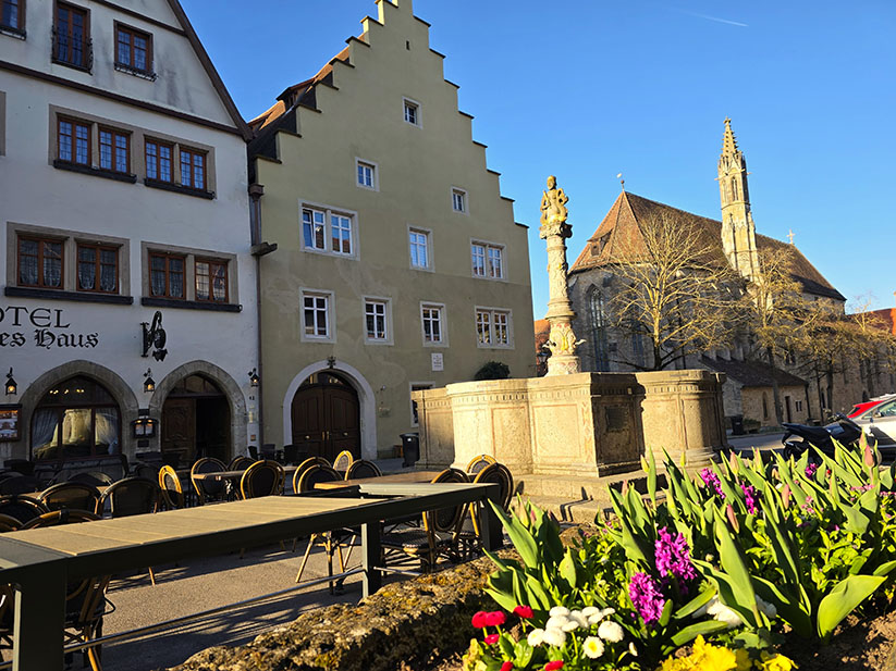 Herrnbrunnen tras una maceta de flores y la iglesia Franziskanerkirche al fondo - Qué ver en Rothenburg