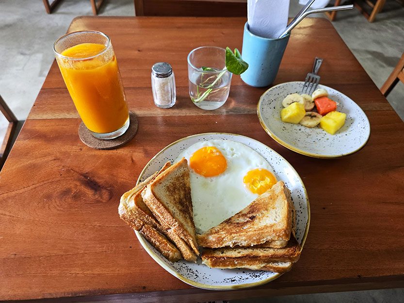 Zumo de mango con plato de fruta y un plato con sandwiches y dos huevos fritos en el medio - Dónde comer en Cartagena de Indias
