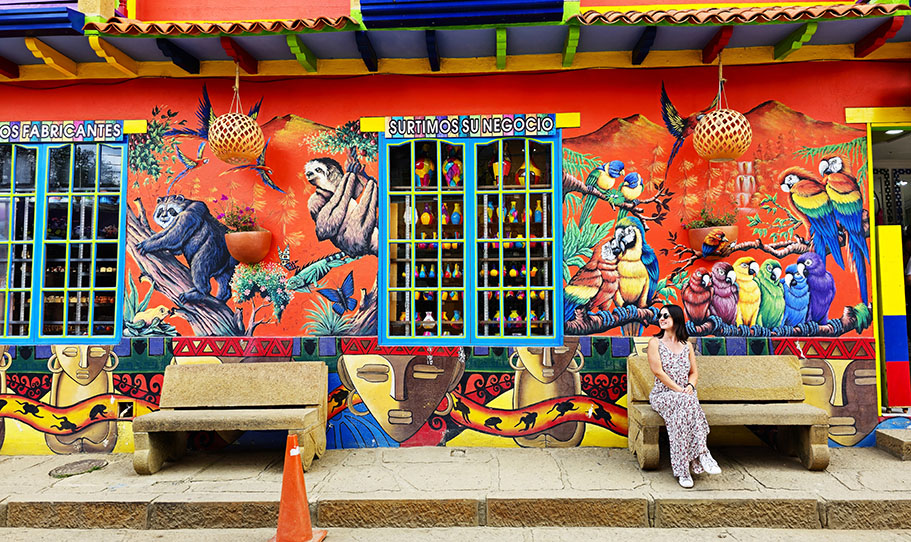 Sentada frente a un mural con loros y más animales en Ráquira - Qué ver en Villa de Leyva