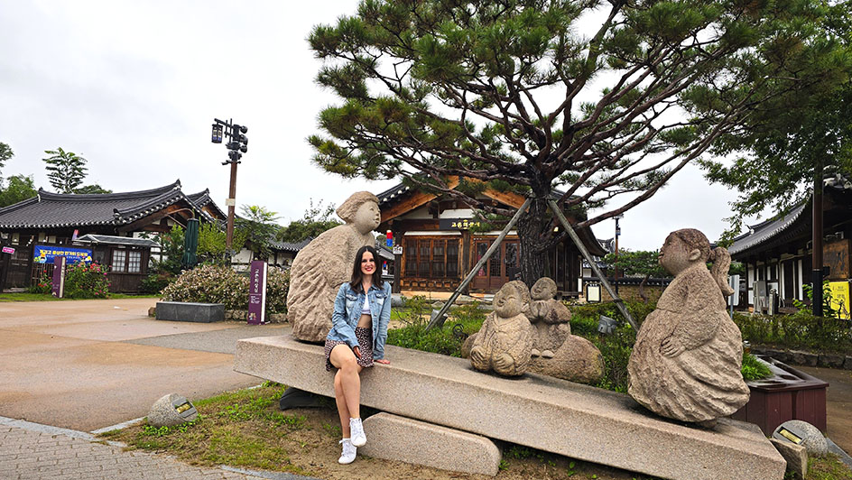 Sentada en un balancín de piedra con figuras de niños coreanos y hanoks al fondo - Qué ver en Gyeongju
