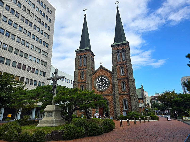 Iglesia de ladrillo con una cruz enfrente entre los árboles - Qué ver en Daegu