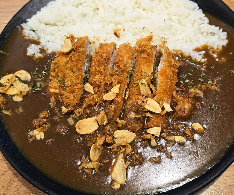 Plato de arroz con cerdo rebozado servido en rebanadas y junto a una salsa marrón - Donkkaseu