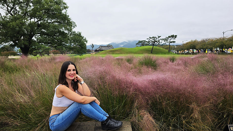 Sentada frente a un campo de hierba muhly de color rosa con los túmulos de fondo - Qué ver en Gyeongju