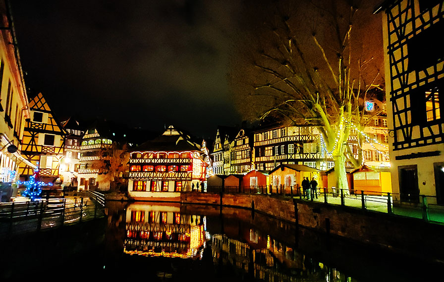 Casas de entramado de madera con un canal enfrente e iluminación navideña - Qué ver en Estrasburgo