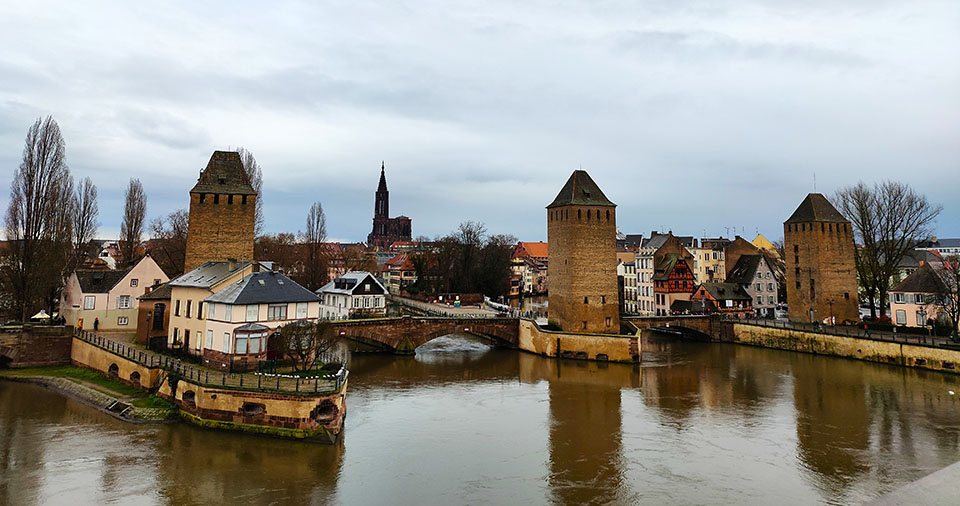 Tres torres atravesadas por un puente con la catedral al fondo. Los Puentes Cubiertos, una de las mejores cosas que ver en Estrasburgo