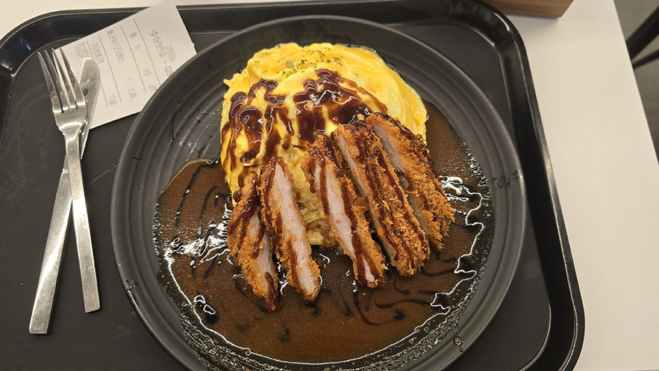 Plato de cerdo rebozado con salsa y una tortilla. Todo colocado en una bandeja negra y con cubiertos - Dónde comer en Seúl