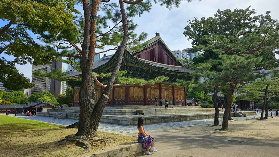 Sentada frente a un palacio, con dos árboles a cada lado - Ruta por Corea del Sur