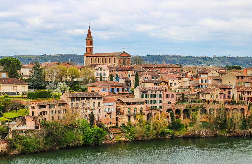Casas de color rojo con una iglesia al fondo. Todo a orillas de un río - Qué ver en Albi