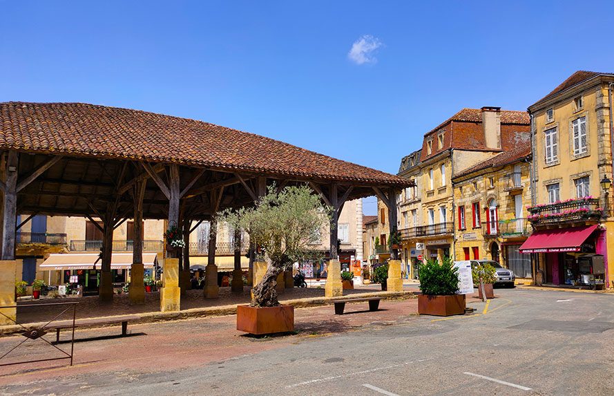 Mercado cubierto de madera con casas de color dorado a la derecha - Los pueblos más bonitos del Périgord Negro (Périgord Noir)