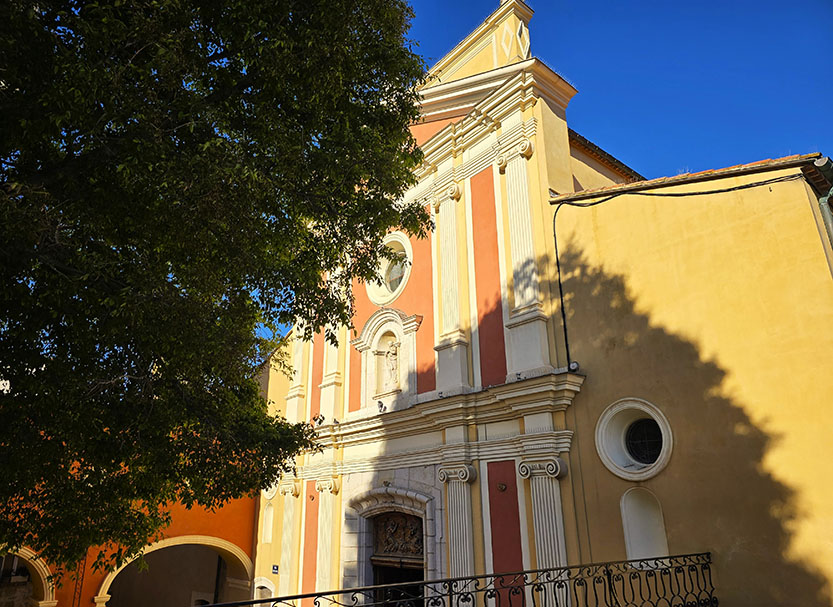 Iglesia de tonos amarillos y granates con un árbol a la izquierda - Qué ver en Antibes