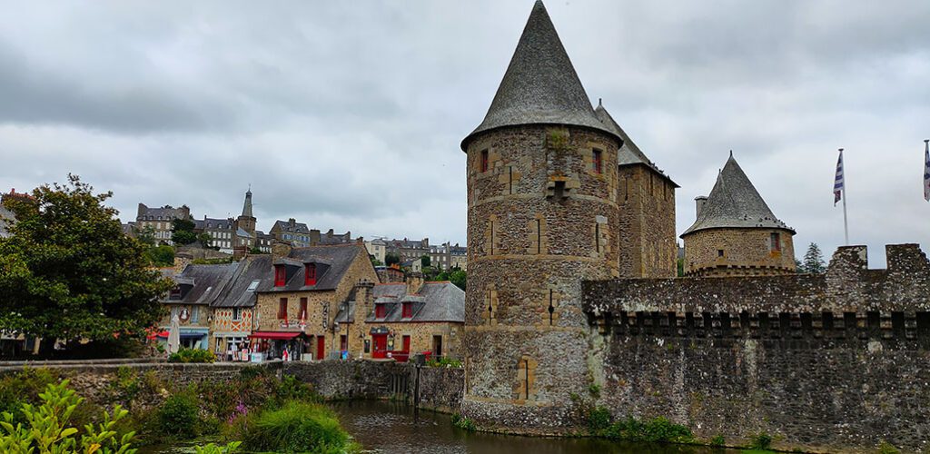 Dos torres con muralla a la derecha y casas de piedra con decoración en rojo - Los pueblos más bonitos de la Bretaña Francesa