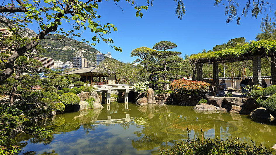 Estanque con árbolrd japoneses a los lados, un puente de pedra blanco enfrente y una casa de te - Qué ver en Mónaco