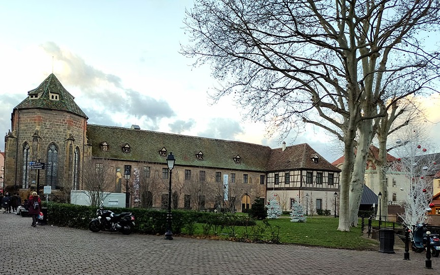 Edificio de piedra con torre a la iquierda y árboles a la derecha - Qué ver en Colmar