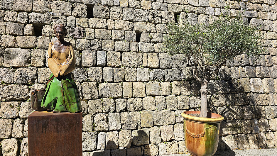 Escultura de Frida Kahlo a la izquierda y un árbol en una maceta a la derecha con pared de piedra - Qué ver en Mougins