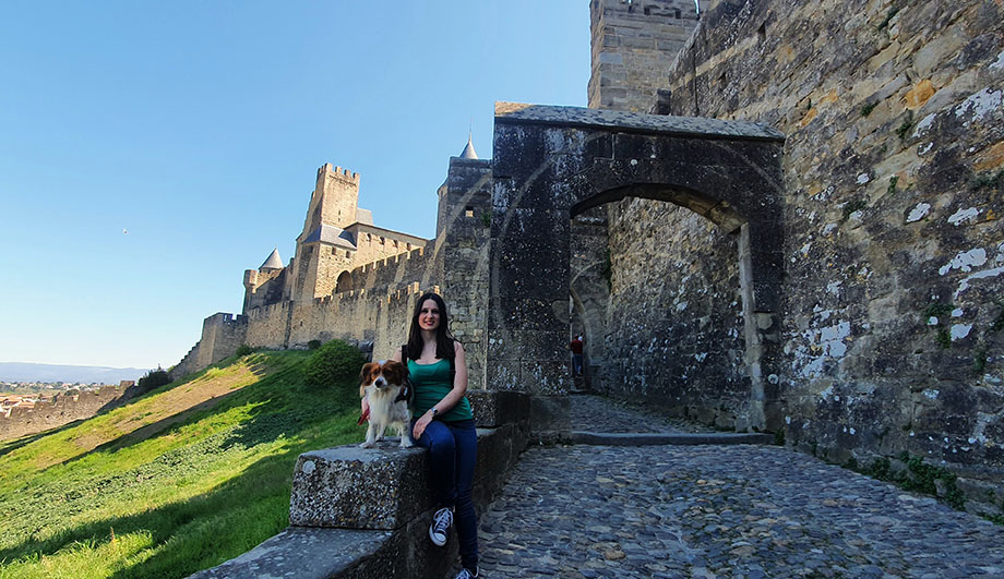 Sentada junto a mi perro frente a una puerta de piedra y las murallas al fondo - Qué ver en Carcassonne