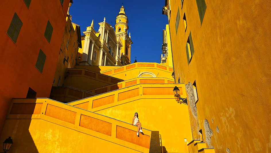 Sentada en una escalinata de color amarillo con una iglesia en lo alto - Qué ver en la Costa Azul