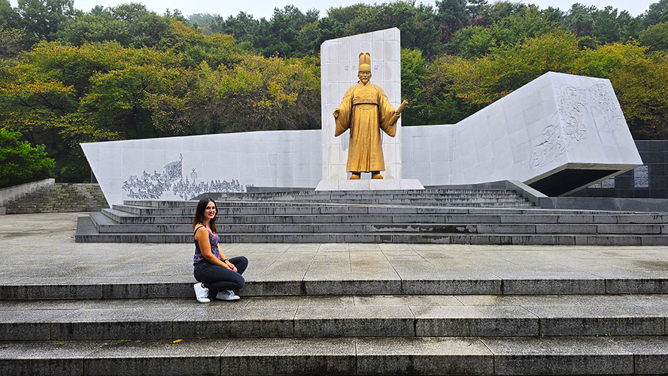 Sentada en unas escaleras con una estatua de oro detrás - Qué ver en Suwon