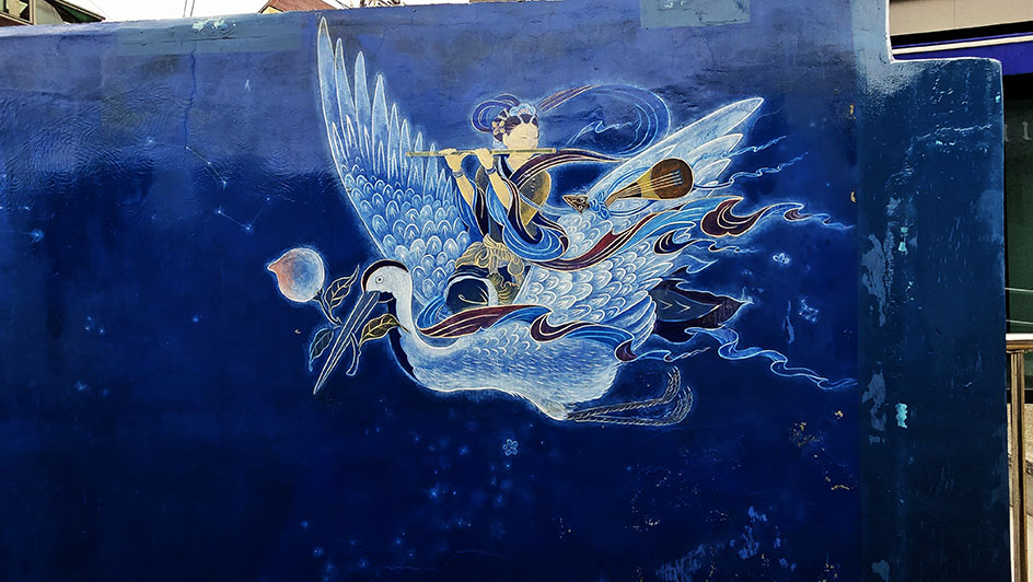Mural con el fondo azulado y un ave llevando a una mujer tocando la flauta - Qué ver en Suwon