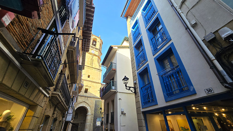 Estrecha calle con edificios abalconados y la torre de una iglesia al fondo - Qué ver en Getaria
