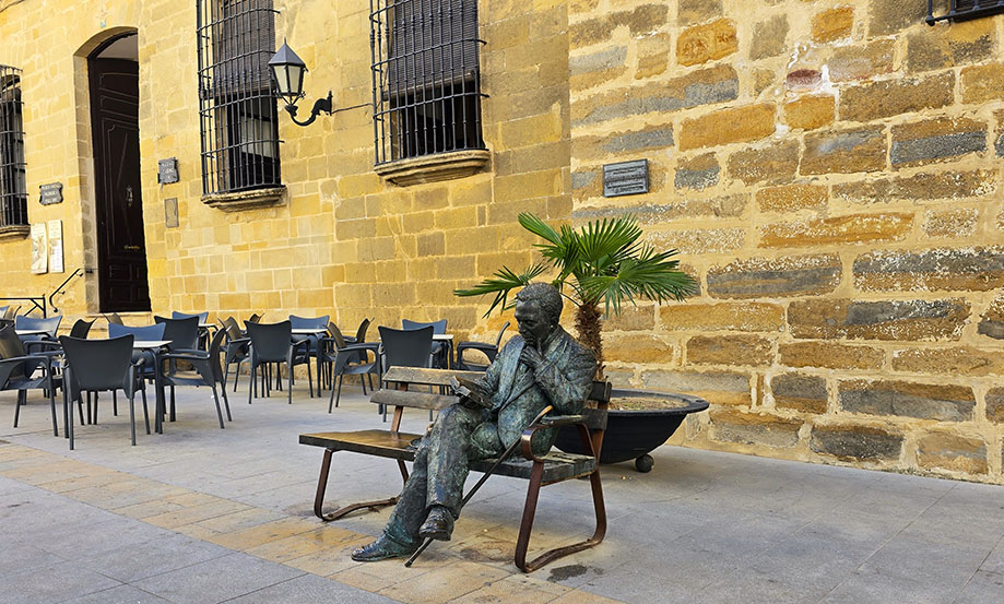 Escultura de Antonio Machado sentado con mesas y sillas a la izquierda - Qué ver en Baeza