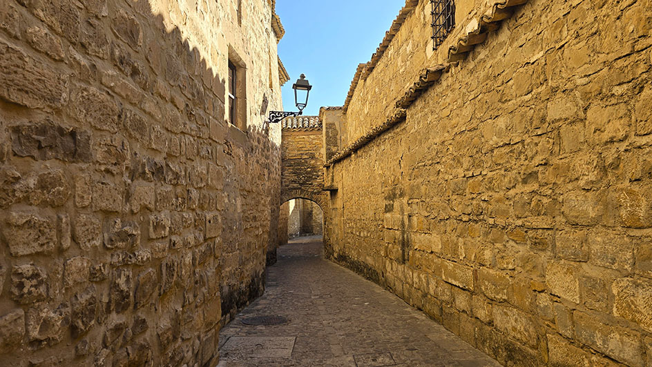 Calle empedrada con un arco y una pequeña farola en la pared izquierda al fondo - Qué ver en Baeza