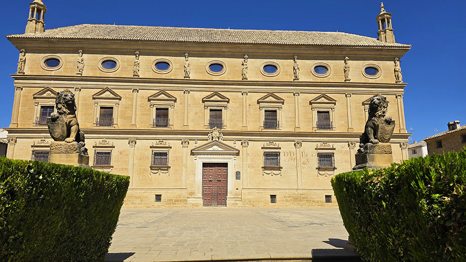 Estatuas de dos leones a cada lado, junto a unos arbustos y enorme palacio de piedra al fondo - Qué ver en Úbeda