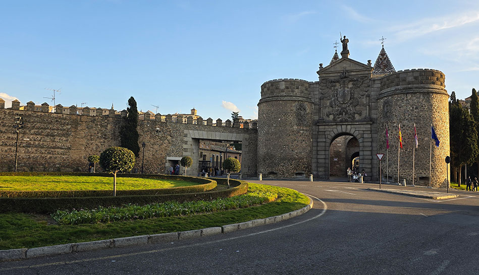 Puerta monumental medieval a la derecha unida a unas murallas con una rotonda enfrente - Qué ver en Toledo