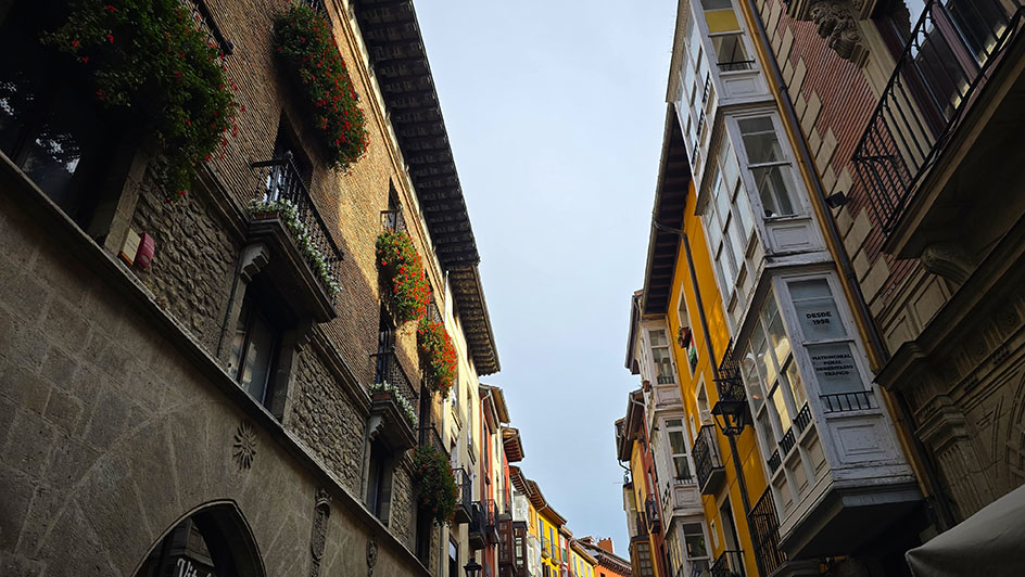 Calle estrecha con un edificio de piedra a la izquierda con balcones llenos de flores y ventanas abalconadas al otro - Qué ver en Vitoria-Gasteiz