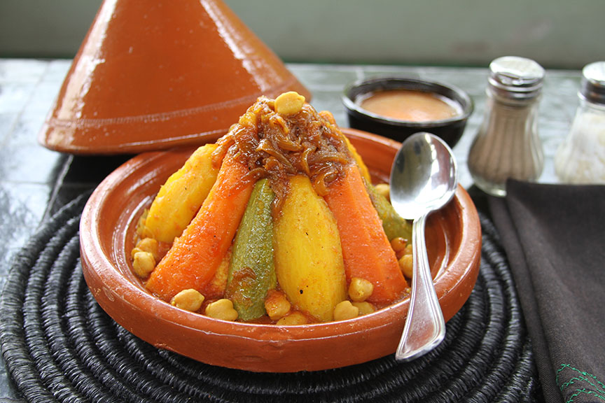 Verdura en piramide con garbanzo abajo en un tajín. Una cuchara a la derecha y sal y pimienta al lado - Qué comer en Marruecos