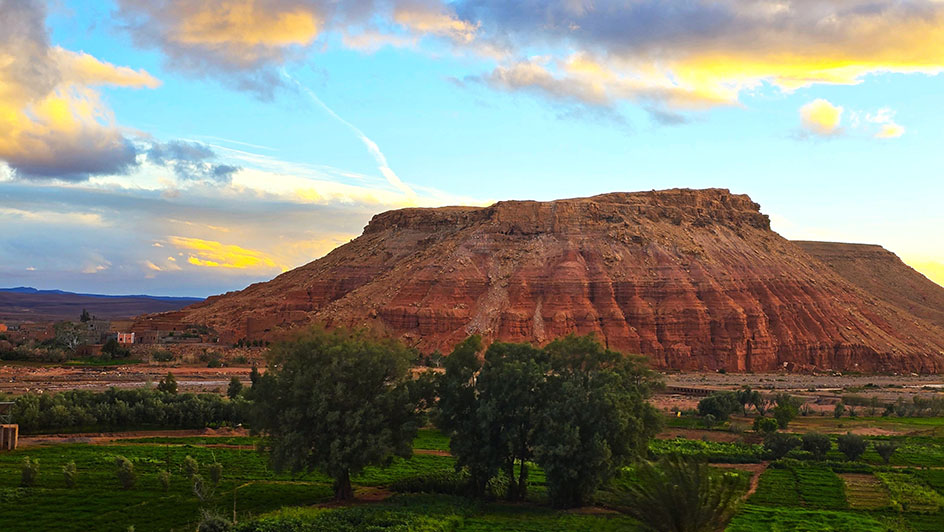 Gran roca de color rojizo con vegetación al frente - Conducir en Marruecos