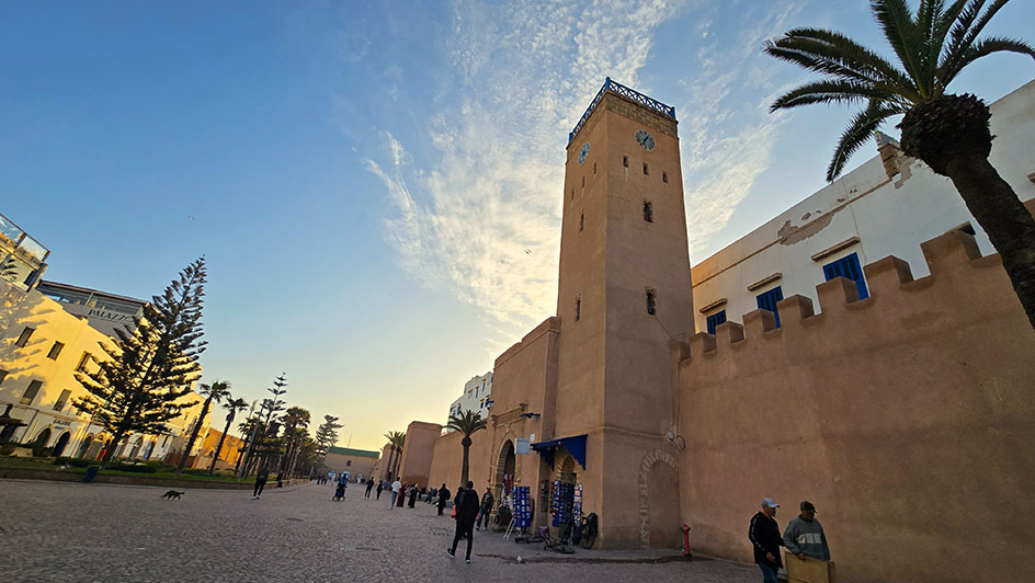 Torre del reloj adherida a las murallas junto a una amplia avenida con árboles a la izquierda - Qué ver en Essaouira