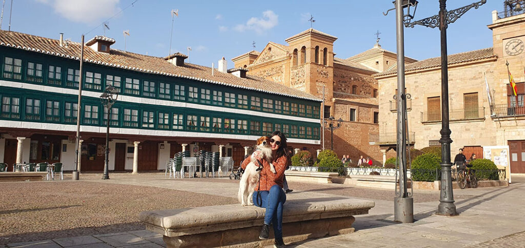 Sentada con mi perro con una plaza detrás con balcones verdes y una iglesia al lado - Qué ver en la Provincia de Ciudad Real