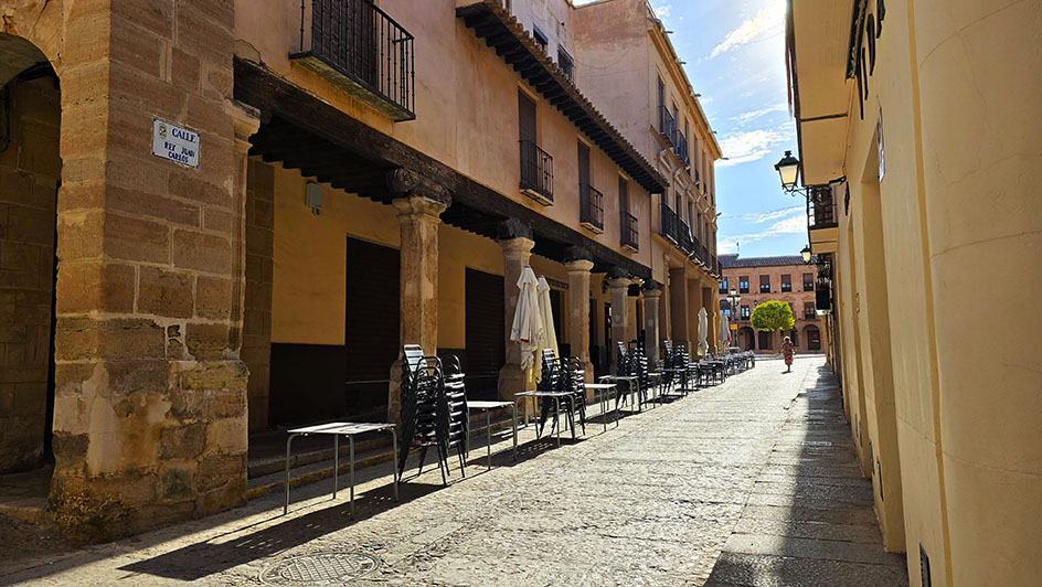 Qué ver en Villanueva de los Infantes: calle empedrada del centro histórico con una zona de soportales distinguida por varias columnas y sillass y mesas al lado
