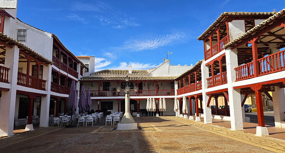 Plaza de dos pisos con balcones de madera rojos y paredes en blanco con una terraza a la izquierda de la plaza - Qué ver en Puerto Lápice