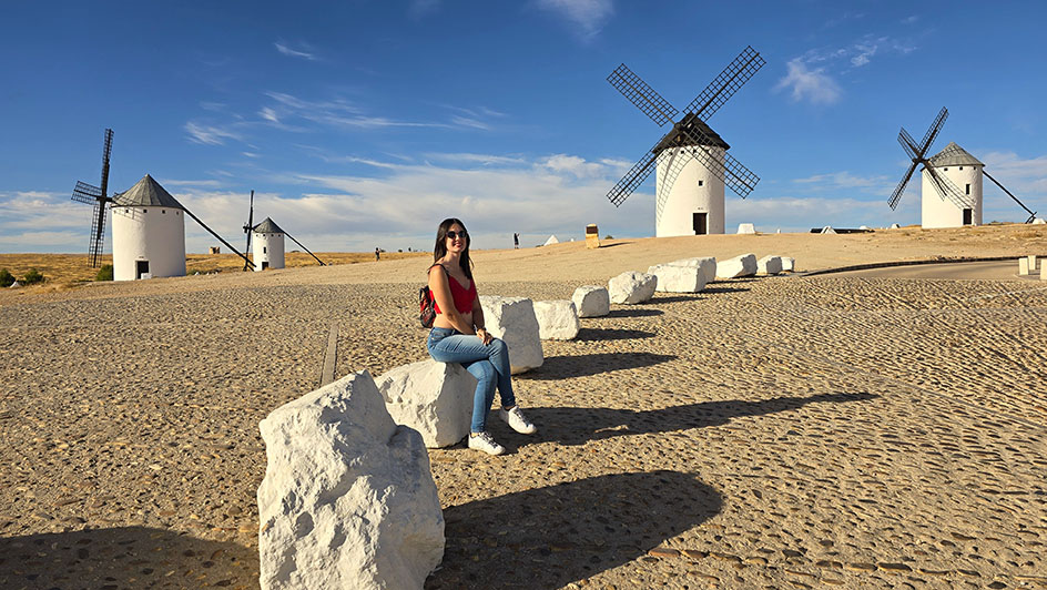 Sentada sobre una piedra blanca con molinos detrás - Qué ver en Campo de Criptana