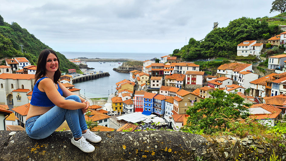 Apoyada con el pueblo pesquero con casas de colores de fondo - Qué ver en Cudillero