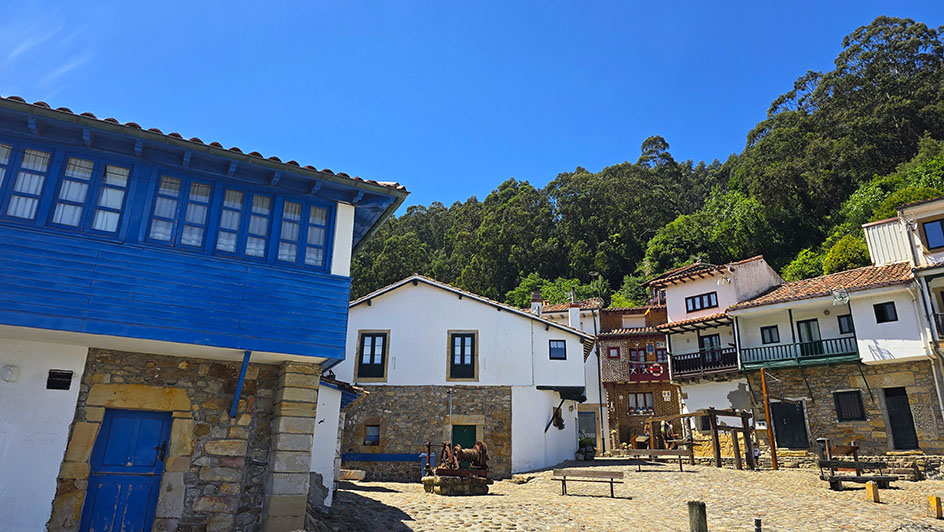 Plaza con casas blancas, empedradas en la parte baja y una a la izquierda con entramado de madera de color azul - Qué ver en Tazones