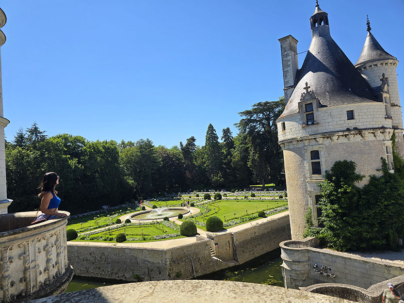 Asomada a un balcón con vistas a una torre y unos jardines con una fuente en medio - Cómo visitar el Castillo de Chenonceau 