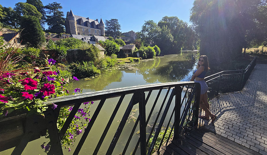 Yo asomada a una barandilla junto a un río con un castillo al fondo y unas flores en el puente a mano izquierda - Qué ver en Montrésor