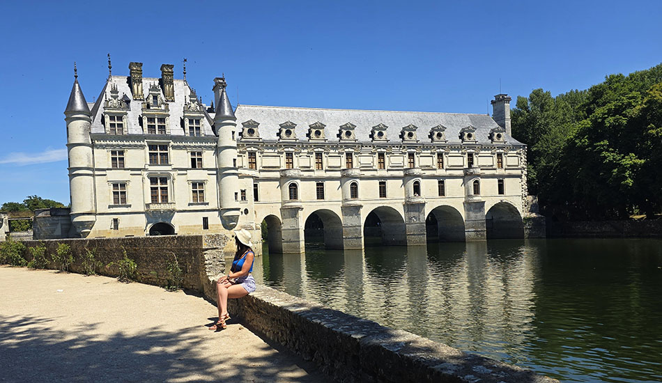 Mujer sentada contemplando el Castillo de Chenonceau sobre el río Cher, uno de los más bonitos que ver en el Valle del Loira