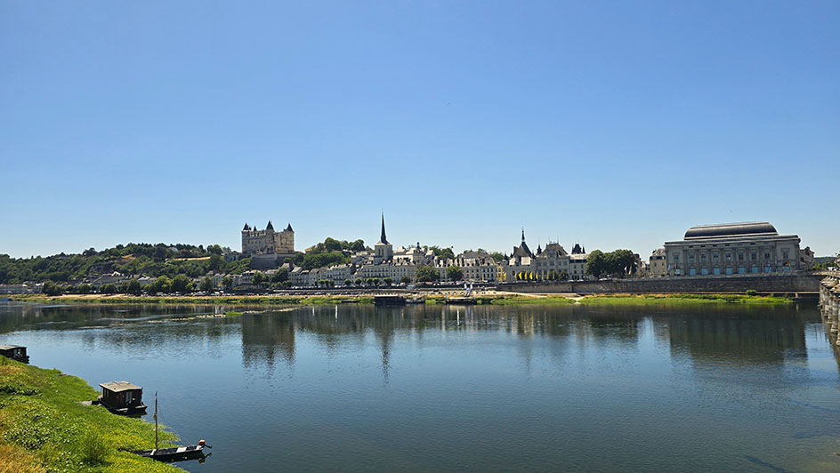 Un río con una pequeña ciudad al fondo donde destaca un castillo con 4 torres - Qué ver en Saumur