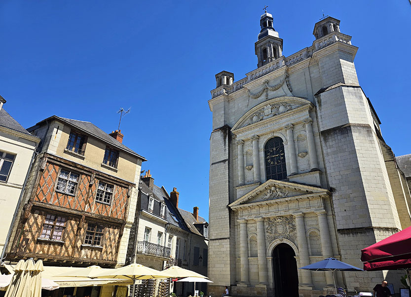 Casa de entramado de madera a la izquierda con una iglesia blanca a la derecha y algunos toldos en la parte baja - Qué ver en Saumur
