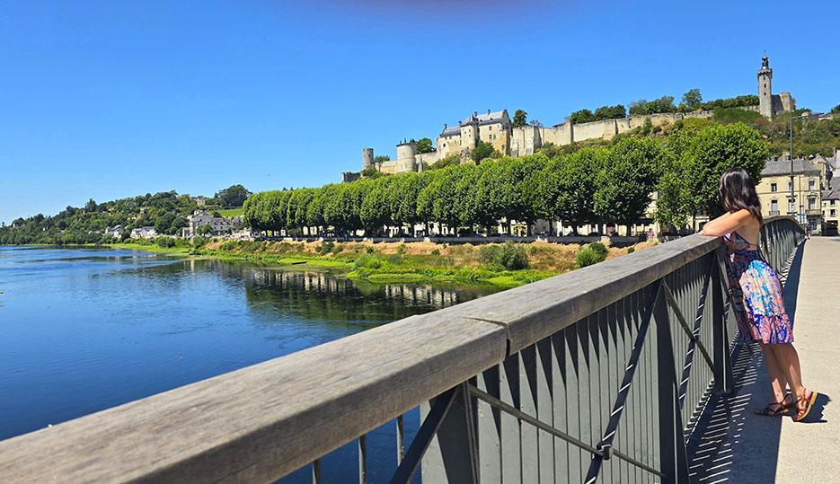 Asomada en un puente viendo una gran fortaleza sobre unos árboles - Qué ver en Chinon