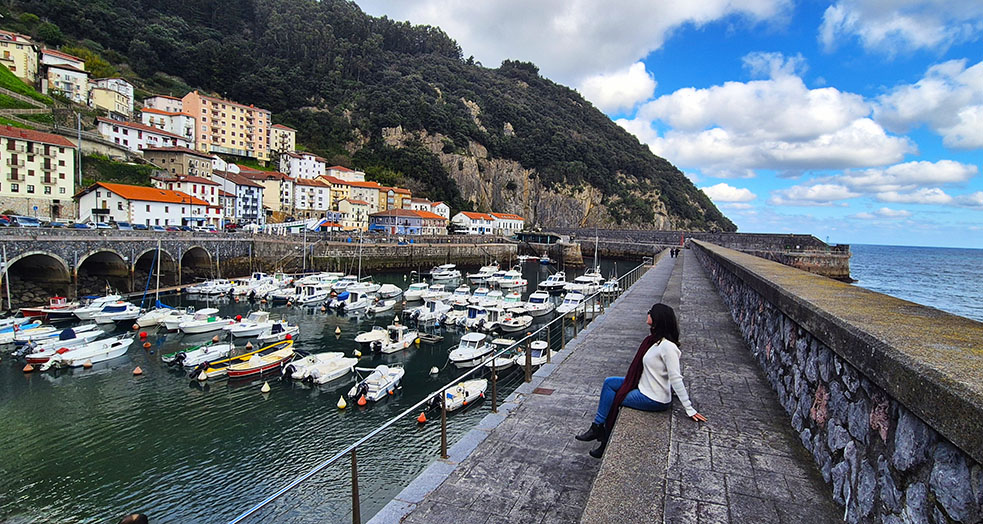 Mujer observando el puerto y las casas coloridas de Elantxobe